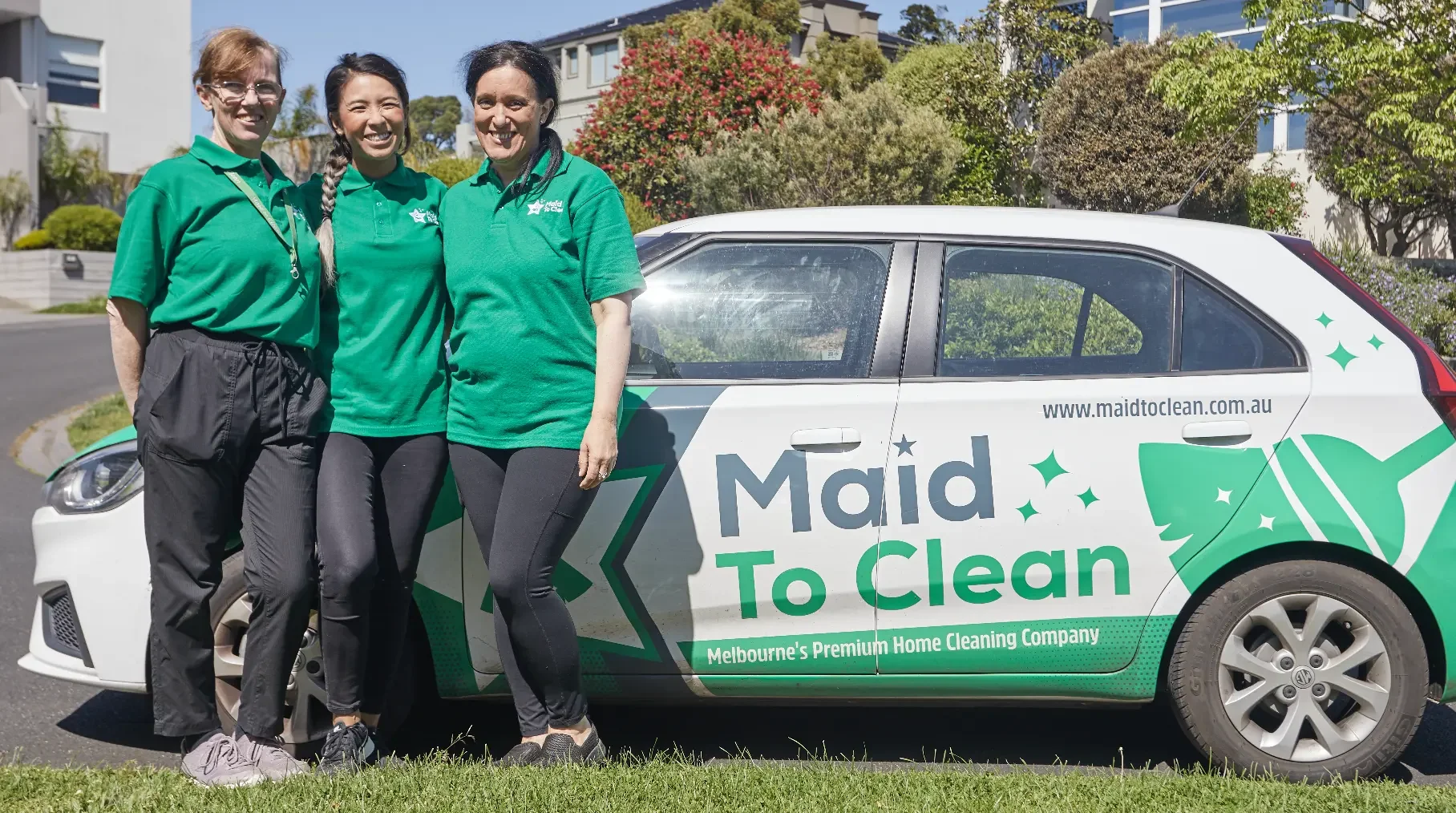 Three Maid to Clean cleaners in green uniforms standing beside the branded Maid to Clean car in a Melbourne street